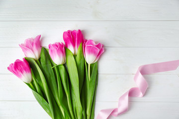 Bouquet of beautiful tulips with color ribbon on white wooden background, top view