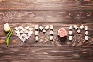 Phrase I LOVE MOM made with white tulip and treats on wooden background, top view. Mother's day composition