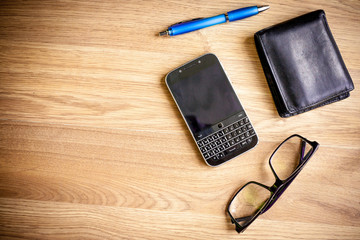Mobile phone, wallet, pen and glasses on a wood grain table