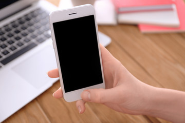 Woman holding smartphone with blank screen at table
