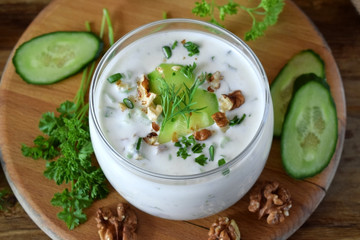 Cold soup with kefir in a glass jar topped with nuts, herbs and cucumber
