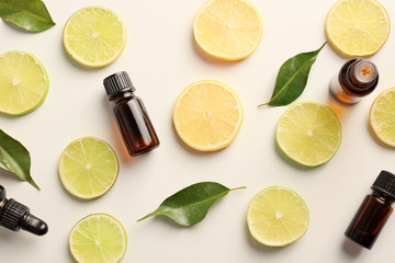 Bottles of essential oils and citrus slices on light background, top view