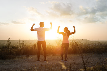Couple of athletes flexing biceps towards the sunset. Couple of athletes celebrating running outdoor workout success.
