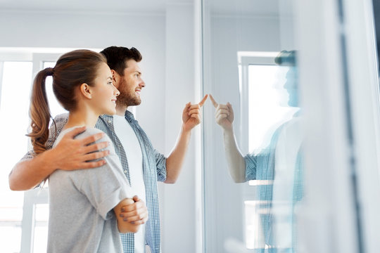mortgage, people and real estate concept - happy couple looking through window or door glass at new home