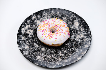 Appetizing donut with sprinkles lie on a black ceramic plate.