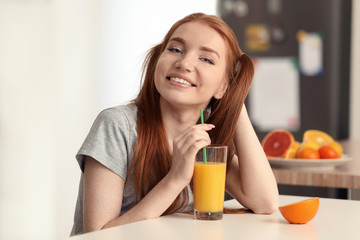 Beautiful young woman drinking citrus juice in kitchen