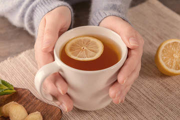 Woman holding cup of hot lemon tea with ginger at table