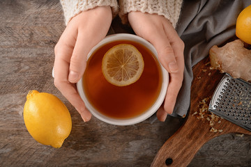 Woman holding cup of hot lemon tea with ginger, top view