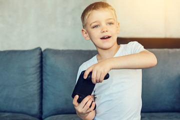 Playful mood. Pleasant little boy involved in games with a new modern games console in his hands