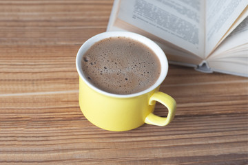 Yellow mug with hot black coffee on a wooden table with an old book.
