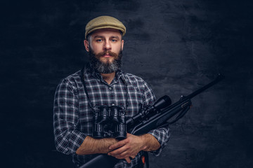 Portrait of a bearded hunter traveler in a fleece shirt and hat holds rifle with a sight and binoculars.