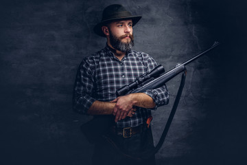 Handsome bearded hunter traveler in a fleece shirt and hat holds rifle with a sight. 