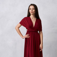 Beautiful long haired young woman dressed in stylish cherry red bandeau maxi dress posing against...