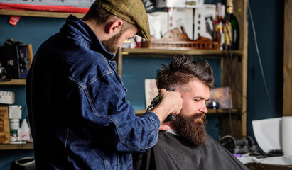 Hipster lifestyle concept. Hipster client getting haircut. Barber with hair clipper works on hairstyle for bearded man barbershop background. Barber with clipper trimming hair on temple of client