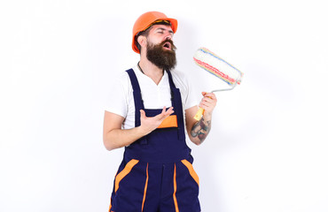 Fun at work. Builder holding paint roller as microphone. Young man singing lyric song over white...