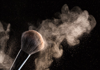 Brush for makeup with flying around powder is isolated on a black background