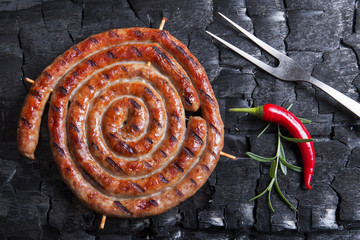 Grilled spiral sausages on a black background of charcoal. 
