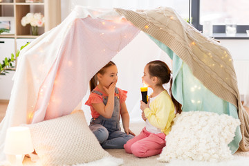 childhood, hygge and friendship concept - little girls with torch light having fun in kids tent or teepee at home © Syda Productions
