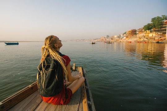 Young Woman Traveler On A Boat Glides Through The Water On Ganges River Along The Shore Of Varanasi, India.