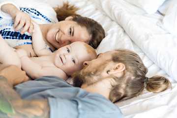 Portrait of happy young parents with baby in the bed at home