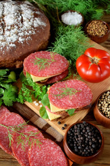 Sandwich with salami, cheese and arugula salad surrounded by the ingredients