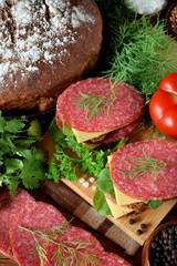 Sandwich with salami, cheese and arugula salad surrounded by the ingredients