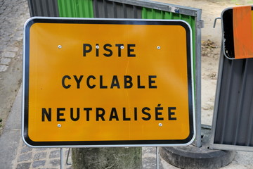 Piste cyclable neutralisée. rue, panneau jaune, lettres noires.
