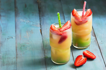 A colorful drink with strawberries on a blue rustic table. Copy space.