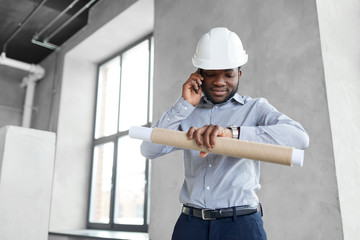 architecture, construction business and people concept - african american architect in helmet with blueprint calling on smartphone and looking at his wristwatch