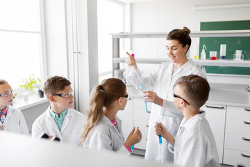 education, science and children concept - teacher and kids or students with test tubes studying chemistry at school laboratory