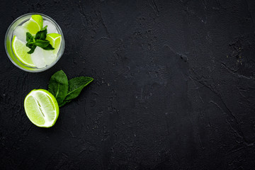 Tropical cocktail. Beverage which women likes. Glass of mojito with slices of lime, mint, ice cubes on black background top view copy space