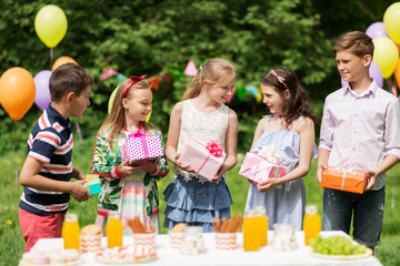 holidays, childhood and celebration concept - happy kids with gifts on birthday party at summer garden