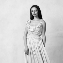 Full body portrait of gorgeous young brunette woman dressed in exquisite nude ball gown with lace top. Attractive female model in elegant strapless dress posing against white wall on background.