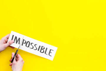 All is possible concept. Hands cutting the part im of written word impossible by sciccors. Yellow background top view copy space