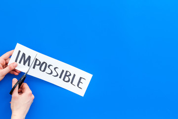 All is possible concept. Hands cutting the part im of written word impossible by sciccors. Blue...