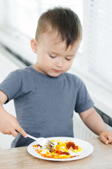 a child in a t-shirt in the kitchen eating an omelet, a fork