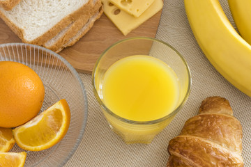 Fresh orange juice in a glass beaker, croissant, sliced orange, banana, cheese, bread. Healthy breakfast.