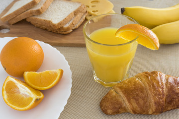 Fresh orange juice in a glass beaker, croissant, sliced orange, banana, cheese, bread. Healthy breakfast.