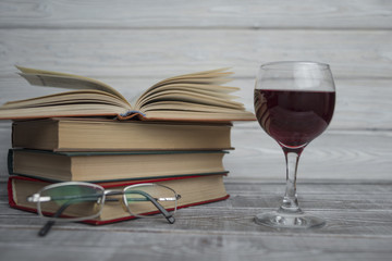 stacked books with glass of wine on a wooden background. Reading Glasses