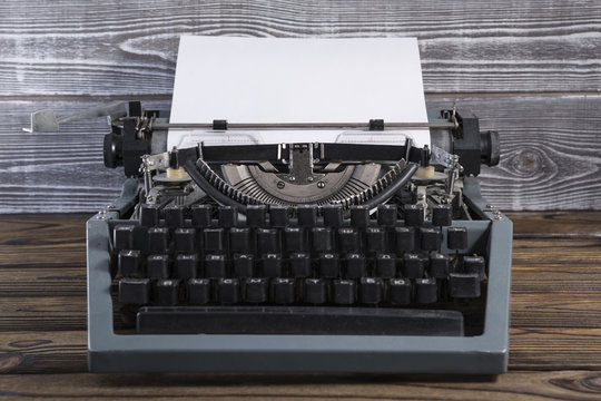 Vintage typewriter with a clean sheet of paper on an old wooden background
