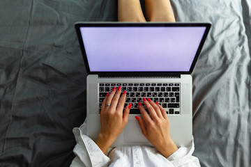 Top view mockup image of a woman sitting on a bed , using and typing on laptop with blank white desktop screen keyboard. Girl blogger is typing for a fresh post