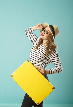 Young happy beautiful woman in hat and funny toy glasses holding yellow suitcase