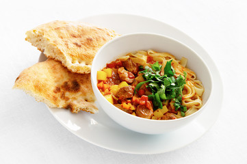 lagman decorated with fresh herbs served with pita