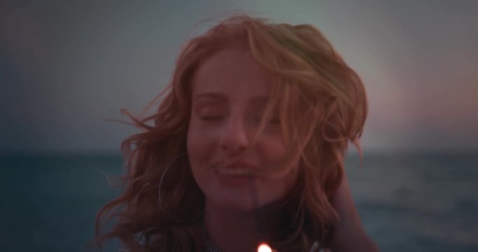 Young redhead hippie woman with sparklers at beach after sunset