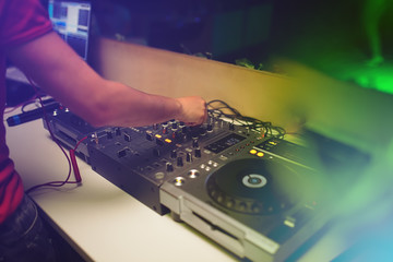 the hands of a young DJ operate a remote in a nightclub creating contemporary music