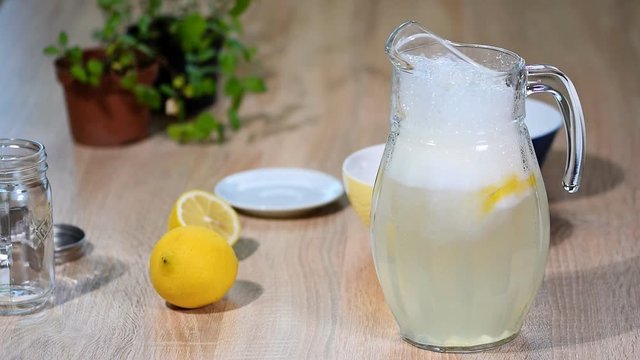 In a jug of lemons pour water. Glass of sparkling water soda drink lemonade with ice and lime lemon slice on white background
