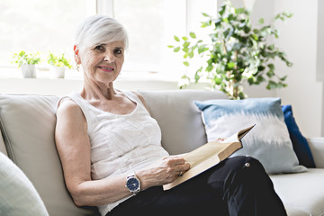 Senior woman reading book at home by fireplace