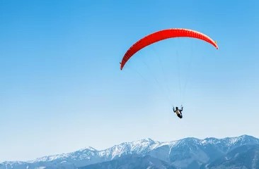 Selbstklebende Fototapete Luftsport Sportler auf rotem Gleitschirm, der über die schneebedeckten Berggipfel fliegt