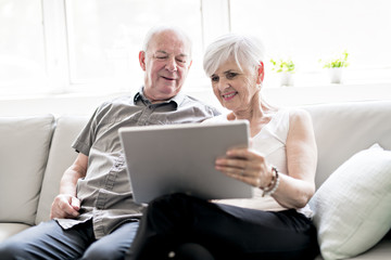 Affectionate attractive elderly couple sitting together on a couch with tablet