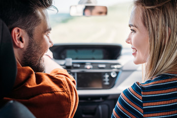 Fototapeta premium side view of smiling couple sitting in car and looking at each other